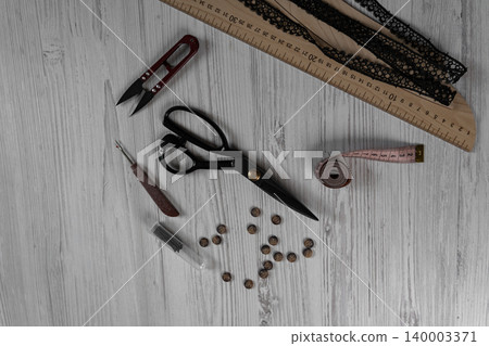 Sewing tools and accessories on table with scissors threads buttons and measuring tape Sewing tools and accessories on table with scissors threads buttons and measuring tape 140003371