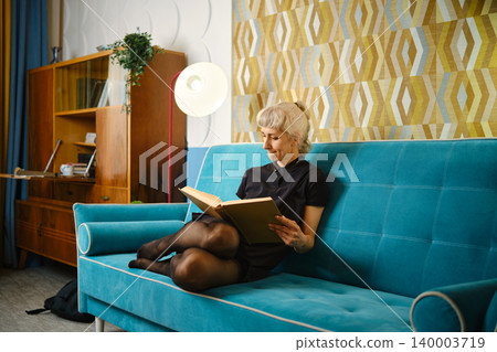 Reading a book while sitting on a turquoise couch in a modern living room during daylight hours Reading a book while sitting on a turquoise couch in a modern living room during daylight hours 140003719