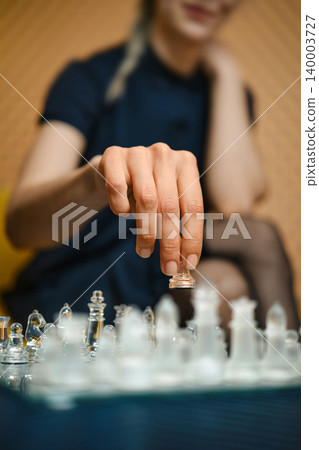Player makes a move on glass chessboard during game in indoor setting in the afternoon Player makes a move on glass chessboard during game in indoor setting in the afternoon 140003727