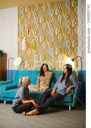 Group of three women chatting on a blue couch in a modern indoor setting during daytime Group of three women chatting on a blue couch in a modern indoor setting during daytime 140003741