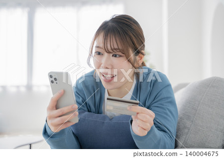 一位女士在沙發上放鬆時看著智慧型手機 一位女士在沙發上放鬆時看著智慧型手機 140004675