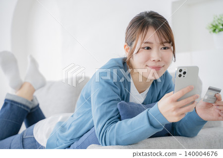 A woman relaxing on a sofa and looking at her smartphone A woman relaxing on a sofa and looking at her smartphone 140004676