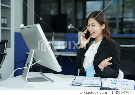 Asian businesswoman talking on mobile phone while working on laptop at office desk. communication, and corporate success. Asian businesswoman talking on mobile phone while working on laptop at office desk. communication, and corporate success. 140004704
