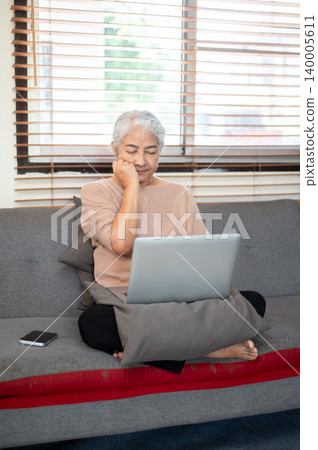 Sleepy old asian woman grandma closing eyes over laptop sitting folding legs on sofa in living room Sleepy old asian woman grandma closing eyes over laptop sitting folding legs on sofa in living room 140005611