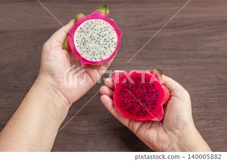 Freshly cut dragon fruit in a woman hands. Slices of delicious pitahaya fruit on wooden background Freshly cut dragon fruit in a woman hands. Slices of delicious pitahaya fruit on wooden background 140005882