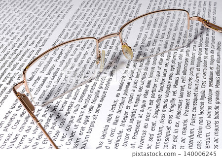 Gold-rimmed spectacles on a sheet of paper with text Gold-rimmed spectacles on a sheet of paper with text 140006245