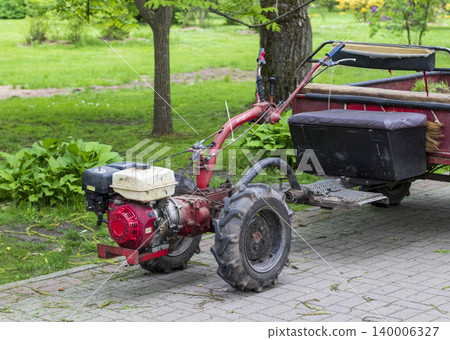 Small agricultural motoblock and cart parked among lush summer trees Small agricultural motoblock and cart parked among lush summer trees 140006327