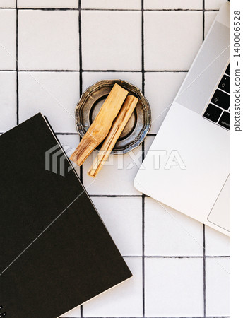 Black notebook, laptop and palo santo sticks in metal dish on tiled background Black notebook, laptop and palo santo sticks in metal dish on tiled background 140006528