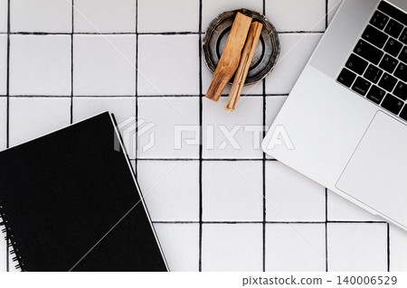 Black notebook, laptop and palo santo sticks in metal dish on tiled background Black notebook, laptop and palo santo sticks in metal dish on tiled background 140006529