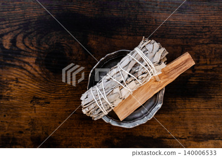 White sage bundle and palo santo stick in ceramic dish on wooden table 140006533