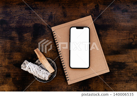 Smartphone with blank screen on notebook with sage and palo santo on wooden table Smartphone with blank screen on notebook with sage and palo santo on wooden table 140006535