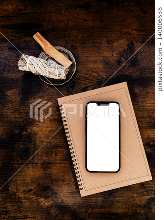 Smartphone with blank screen on notebook with sage and palo santo on wooden table Smartphone with blank screen on notebook with sage and palo santo on wooden table 140006536