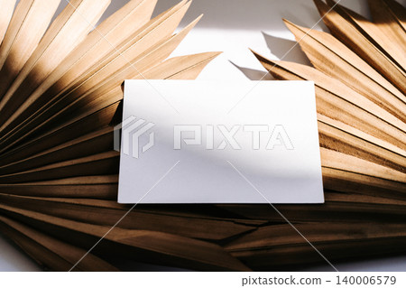 Blank white business card mockup on dried palm leaves background with warm natural light 140006579