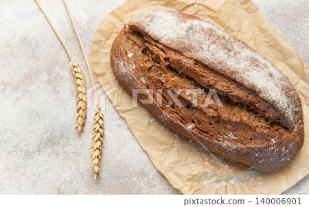 Rye bread loaf with wheat ears on parchment paper Rye bread loaf with wheat ears on parchment paper 140006901