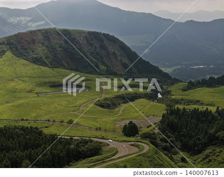 An aerial photograph capturing the green grasslands and winding roads of Minami Aso, Kumamoto Prefecture. An aerial photograph capturing the green grasslands and winding roads of Minami Aso, Kumamoto Prefecture. 140007613