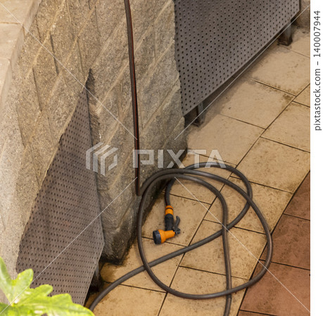 Coiled Garden Hose with Spray Nozzle on Atrium Tiled Floor. Household Coiled Garden Hose with Spray Nozzle on Atrium Tiled Floor. Household 140007944