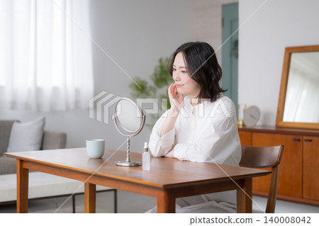 一位女士在客廳裡對著鏡子進行護膚時面帶微笑，體現了一種精緻的生活方式和美麗與生活理念。 140008042