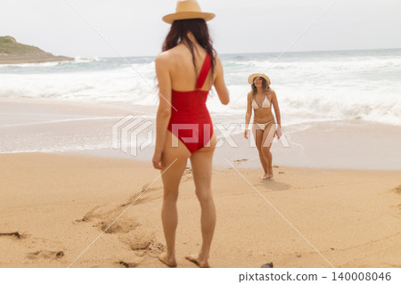 Women enjoying their time at the beach while walking on the sand near the ocean during a cloudy day Women enjoying their time at the beach while walking on the sand near the ocean during a cloudy day 140008046
