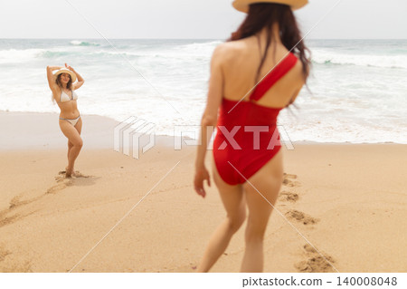 Friends enjoying time at the beach while walking on sand and playing near the waves in sunny weather 140008048