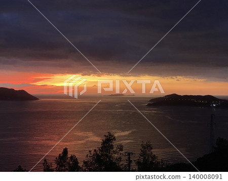 Sunset over calm sea with silhouetted trees and distant islands, ideal for background use 140008091