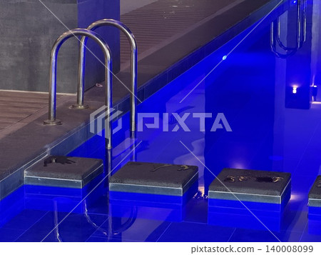 Blue ambient lighting illuminating indoor swimming pool ladder and tiled lanes at night background Blue ambient lighting illuminating indoor swimming pool ladder and tiled lanes at night background 140008099