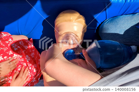 First aid training with CPR mannequin. Medical students practicing cardiopulmonary resuscitation and using an Ambu bag mask for artificial ventilation during a first aid seminar. 140008156