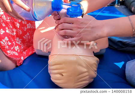 First aid training with CPR mannequin. Medical students practicing cardiopulmonary resuscitation and using an Ambu bag mask for artificial ventilation during a first aid seminar. 140008158