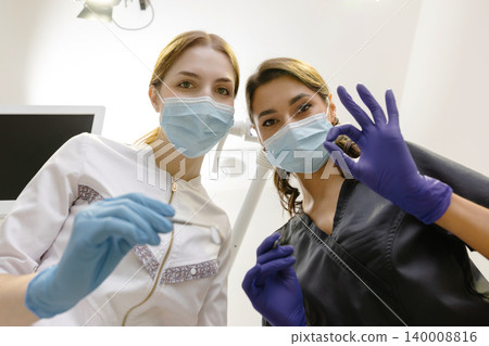 From below female dentists with mirror and device bending over patient during appointment in dental clinic From below female dentists with mirror and device bending over patient during appointment in dental clinic 140008816