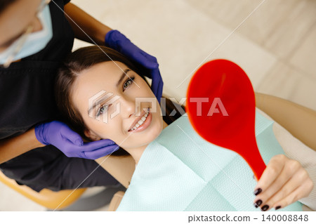 Girl is sitting in a dental chair in a dentist's office. The dentist checks the patient's condition by touching her head Girl is sitting in a dental chair in a dentist's office. The dentist checks the patient's condition by touching her head 140008848
