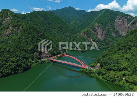 An aerial photograph overlooking the red arch bridge spanning the Hyugami Dam in Yame City, Fukuoka Prefecture. An aerial photograph overlooking the red arch bridge spanning the Hyugami Dam in Yame City, Fukuoka Prefecture. 140009628