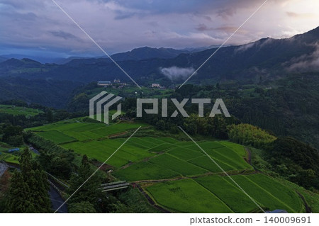 An aerial photograph taken at sunset, capturing the terraced rice fields and misty mountain range in Hinokage Town, Kumamoto Prefecture. An aerial photograph taken at sunset, capturing the terraced rice fields and misty mountain range in Hinokage Town, Kumamoto Prefecture. 140009691