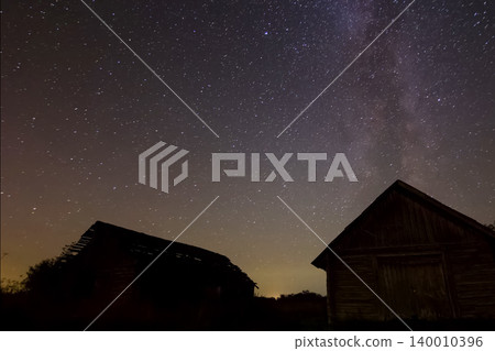 Starry sky over wooden houses in the village. Starry sky background picture of stars in night sky and the Milky Way. 140010396