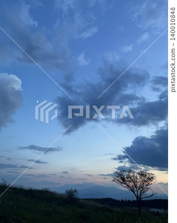 月亮懸浮在雲層之上，夕陽西下。 140010848