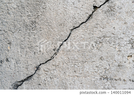 Cracked Concrete Wall. Gray concrete wall texture with visible crack running diagonally across a rough cement surface. Natural as background, backdrop, concrete mockup for construction themes Cracked Concrete Wall. Gray concrete wall texture with visible crack running diagonally across a rough cement surface. Natural as background, backdrop, concrete mockup for construction themes 140011094