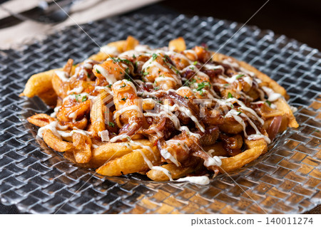 Loaded french fries with chicken, caramelized onion and sauce served on glass plate Loaded french fries with chicken, caramelized onion and sauce served on glass plate 140011274