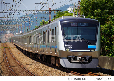 小田急5000系列車在綠樹成蔭的郊區筆直的鐵軌上飛馳。 小田急5000系列車在綠樹成蔭的郊區筆直的鐵軌上飛馳。 140012237