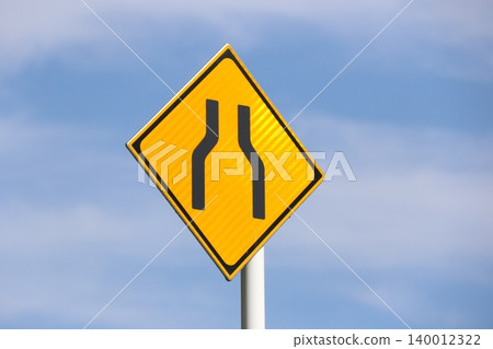 A warning sign (road sign) indicating a "narrowing of road width" against a blue sky. A warning sign (road sign) indicating a "narrowing of road width" against a blue sky. 140012322