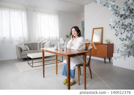 A woman enjoying a mindful lifestyle in her living room, smiling as she looks in the mirror while doing her skincare routine, and her focus on beauty and a natural lifestyle. A woman enjoying a mindful lifestyle in her living room, smiling as she looks in the mirror while doing her skincare routine, and her focus on beauty and a natural lifestyle. 140012376