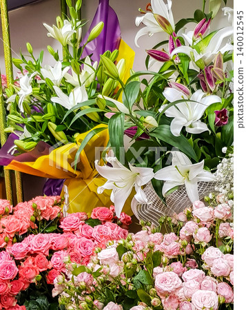 Colorful floral arrangement featuring white lilies and pink roses with decorative wrapping in a flower shop setting, vibrant colors and textures visible 140012545