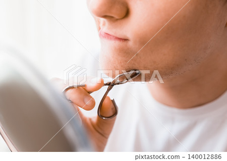 A woman looks in a mirror, using tweezers for facial hair removal on her chin to manage unwanted hair and hormonal changes in her daily home beauty routine. A woman looks in a mirror, using tweezers for facial hair removal on her chin to manage unwanted hair and hormonal changes in her daily home beauty routine. 140012886