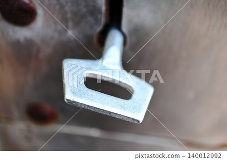Garage Door Key in Lock Tight Macro, Worn Silver Hardware Detail Against Weathered Rust Spotted Surface 140012992