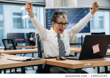 Excited businesswoman celebrating success at her desk in a modern office environment, showcasing enthusiasm and achievement in the workplace Excited businesswoman celebrating success at her desk in a modern office environment, showcasing enthusiasm and achievement in the workplace 140014141