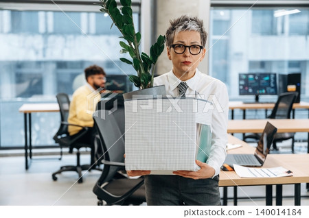 Businesswoman carrying a plant in a box while standing in a modern office environment, showcasing a fresh start and organizational change in the workplace Businesswoman carrying a plant in a box while standing in a modern office environment, showcasing a fresh start and organizational change in the workplace 140014184