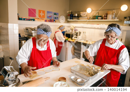 Senior African American and Caucasian women chefs preparing pastries in a professional kitchen bakery Senior African American and Caucasian women chefs preparing pastries in a professional kitchen bakery 140014194