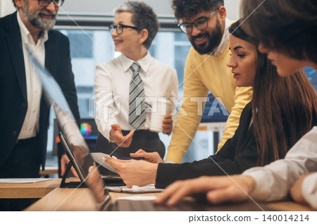 Group of diverse professionals collaborating in a modern office setting, discussing ideas and strategies around a laptop, showcasing teamwork and innovation 140014214