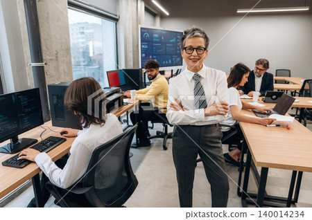 Confident businesswoman stands in modern office, surrounded by colleagues working on computers, showcasing teamwork and collaboration in a professional environment Confident businesswoman stands in modern office, surrounded by colleagues working on computers, showcasing teamwork and collaboration in a professional environment 140014234
