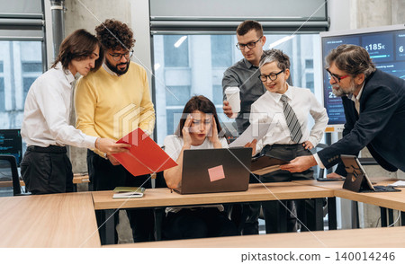 Group of diverse business professionals collaborating in modern office, analyzing data on laptop, surrounded by documents and technology, showcasing teamwork and problem-solving Group of diverse business professionals collaborating in modern office, analyzing data on laptop, surrounded by documents and technology, showcasing teamwork and problem-solving 140014246