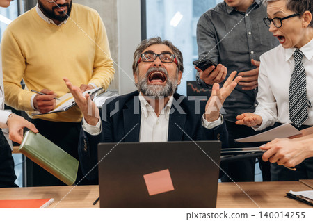 Businessman in office expressing frustration while surrounded by colleagues discussing tasks, showcasing workplace dynamics and stress management Businessman in office expressing frustration while surrounded by colleagues discussing tasks, showcasing workplace dynamics and stress management 140014255