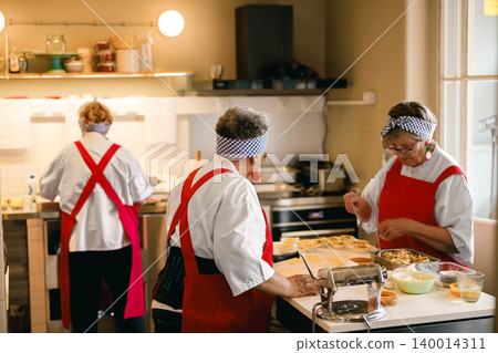 Diverse Senior Women Chefs Preparing Pastries in a Professional Commercial Kitchen Bakery Diverse Senior Women Chefs Preparing Pastries in a Professional Commercial Kitchen Bakery 140014311