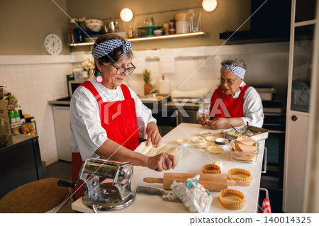 Active senior Caucasian and Black women preparing pastries in a bright commercial kitchen Active senior Caucasian and Black women preparing pastries in a bright commercial kitchen 140014325